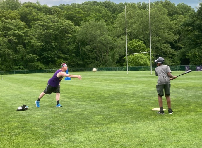 Photo of a coach pitching a beep baseball to an athlete